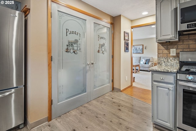 kitchen with tasteful backsplash, gray cabinets, light hardwood / wood-style floors, and appliances with stainless steel finishes