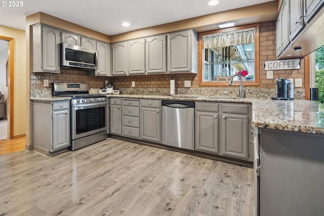 kitchen with gray cabinets, appliances with stainless steel finishes, sink, decorative backsplash, and light hardwood / wood-style flooring