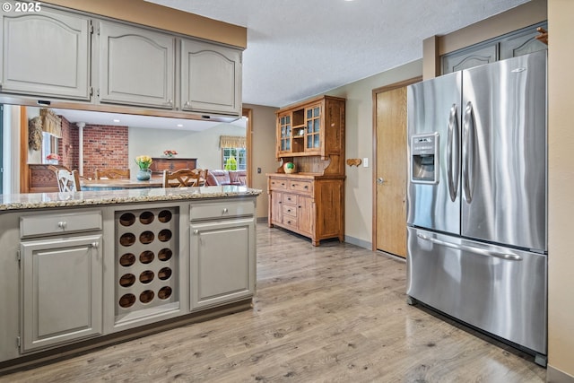 kitchen featuring stainless steel fridge with ice dispenser, light stone countertops, a textured ceiling, and light wood-type flooring