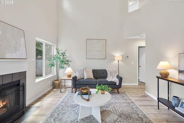 17848 SW Eldred Ln, Sherwood, OR 97140 - living room featuring a towering ceiling, a tiled fireplace, baseboards, and light wood-style floors