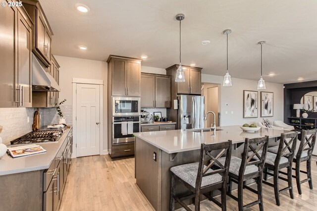 4747 S 17th Dr, Ridgefield, WA 98642 - kitchen with appliances with stainless steel finishes, a kitchen breakfast bar, an island with sink, under cabinet range hood, and backsplash
