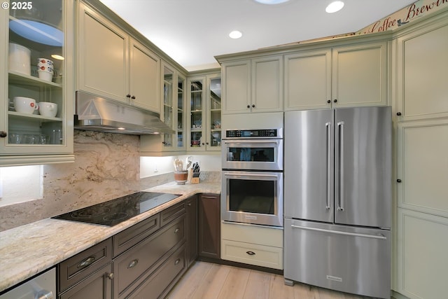 kitchen with light stone countertops, appliances with stainless steel finishes, light wood-style floors, tasteful backsplash, and under cabinet range hood