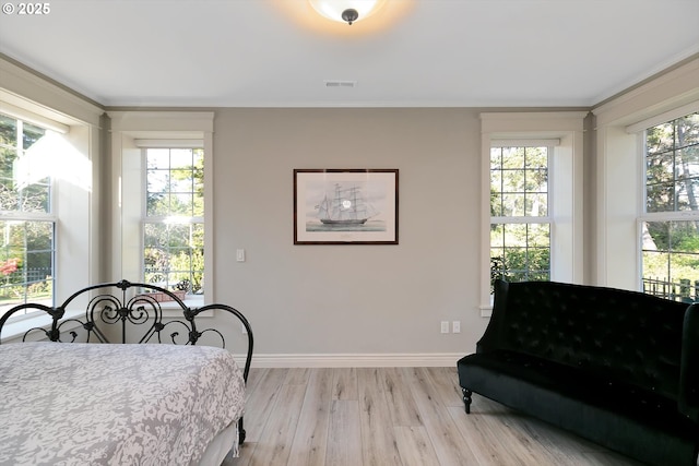 bedroom with baseboards, ornamental molding, light wood-type flooring, and visible vents