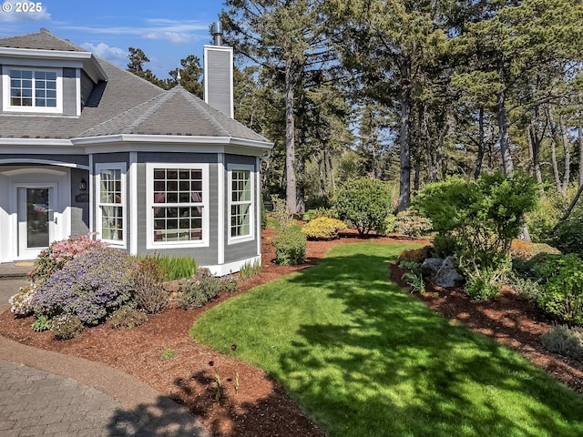 view of side of home featuring a yard, a chimney, and a shingled roof