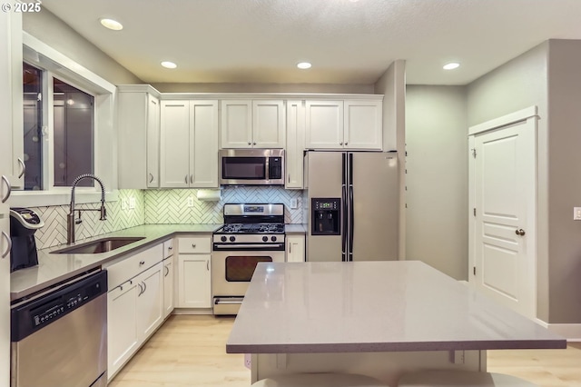 kitchen featuring appliances with stainless steel finishes, a sink, light wood finished floors, a kitchen island, and white cabinetry