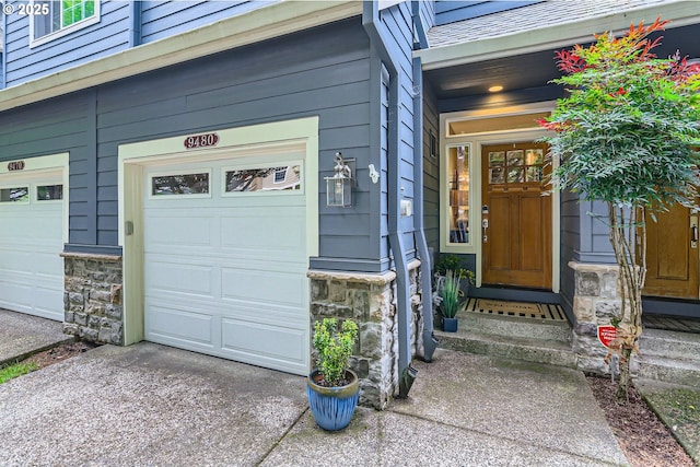 property entrance featuring stone siding, an attached garage, and driveway