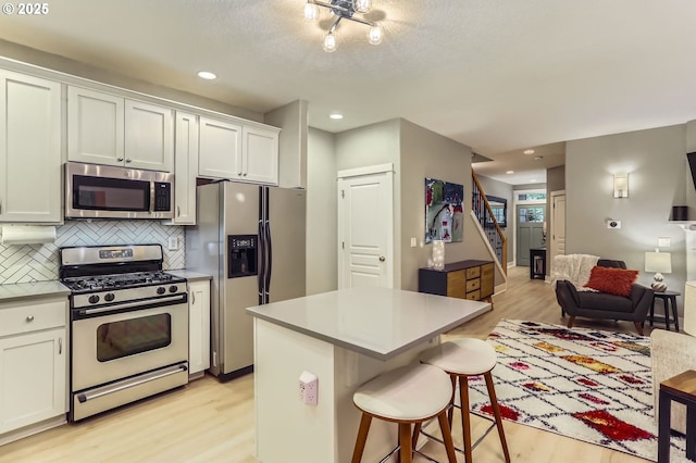 9480 SW 153rd Ave, Beaverton, OR 97007 - kitchen featuring appliances with stainless steel finishes, light wood finished floors, tasteful backsplash, a kitchen breakfast bar, and a center island