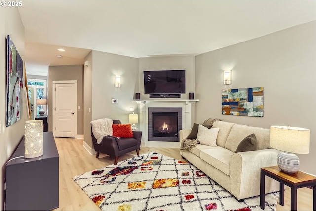 living room with light wood-style flooring, a warm lit fireplace, recessed lighting, and baseboards