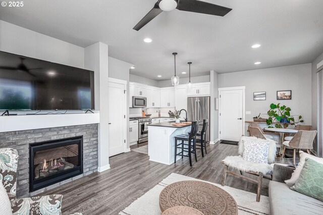 living area featuring a glass covered fireplace, baseboards, dark wood-style floors, recessed lighting, and a ceiling fan