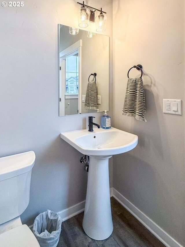 bathroom featuring baseboards, wood finished floors, and toilet