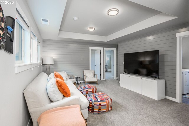 living room featuring washer / clothes dryer, visible vents, wood walls, a tray ceiling, and carpet flooring