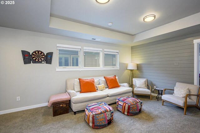 living room featuring carpet flooring, wood walls, baseboards, a tray ceiling, and visible vents