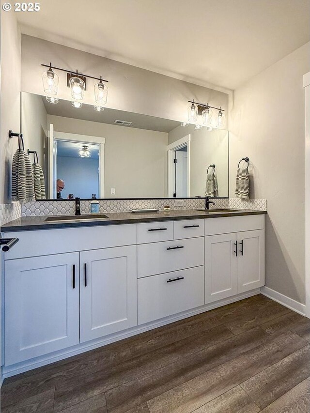 bathroom featuring visible vents, double vanity, wood finished floors, tasteful backsplash, and a sink