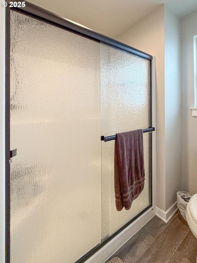 full bath featuring baseboards, a shower stall, toilet, and wood finished floors