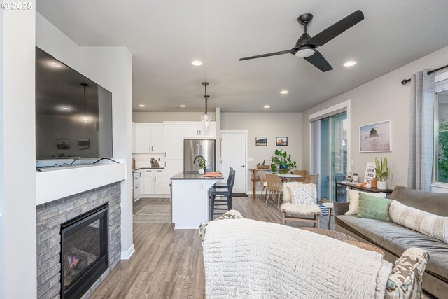 living area featuring light wood-type flooring, recessed lighting, ceiling fan, and a fireplace