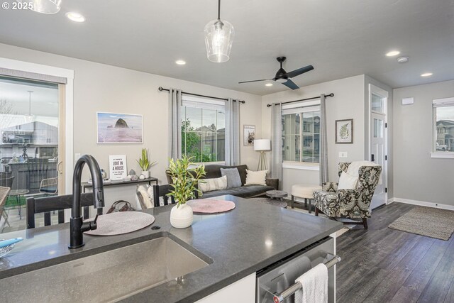 kitchen with dark countertops, a sink, dark wood finished floors, recessed lighting, and stainless steel dishwasher