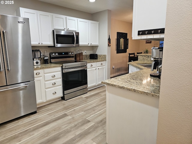 kitchen with recessed lighting, light stone counters, light wood finished floors, white cabinetry, and appliances with stainless steel finishes