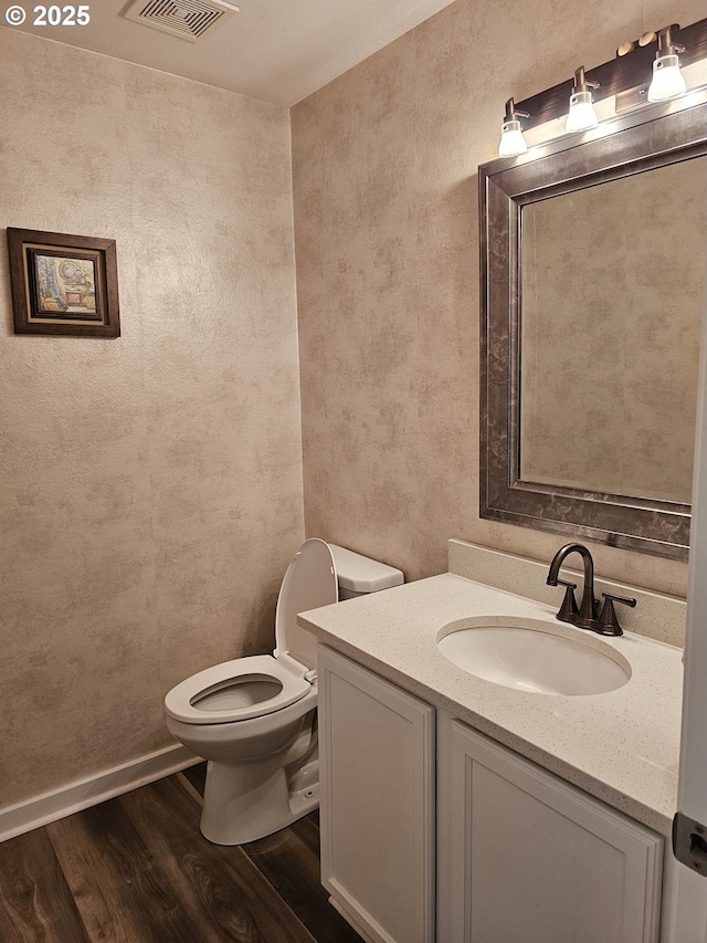 half bath featuring toilet, visible vents, wood finished floors, and vanity