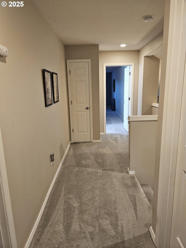 hallway with carpet flooring, a textured ceiling, and baseboards