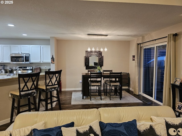 dining space with dark wood-style flooring, a textured ceiling, baseboards, and recessed lighting