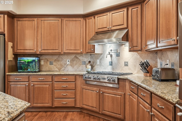 kitchen with range hood, backsplash, hardwood / wood-style flooring, light stone counters, and stainless steel appliances