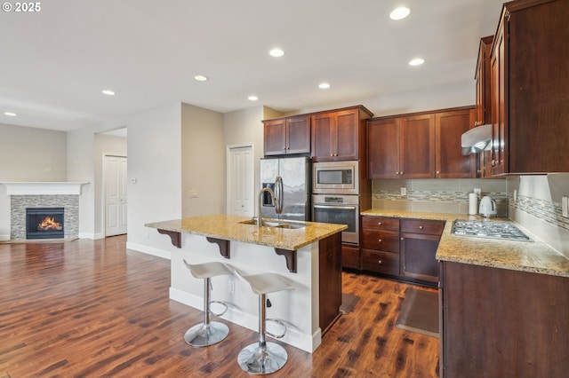 kitchen featuring sink, light stone counters, appliances with stainless steel finishes, a kitchen island with sink, and decorative backsplash