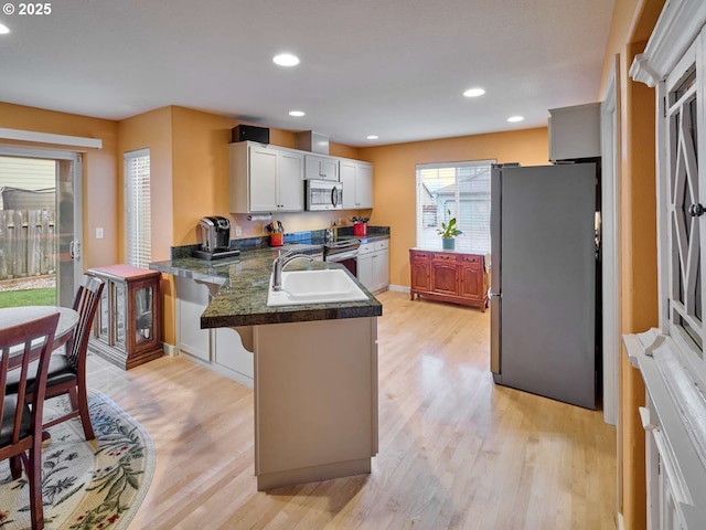 kitchen featuring a breakfast bar area, light wood finished floors, a peninsula, a sink, and appliances with stainless steel finishes