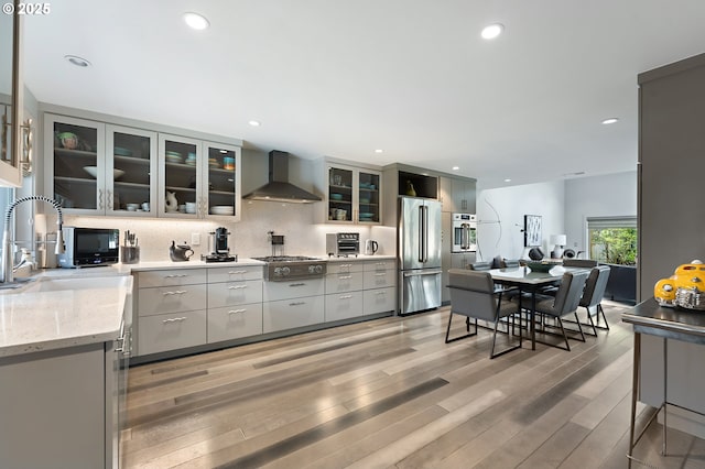 240 Greenridge Dr, Lake Oswego, OR 97035 - kitchen with wall chimney range hood, appliances with stainless steel finishes, light wood finished floors, tasteful backsplash, and gray cabinets