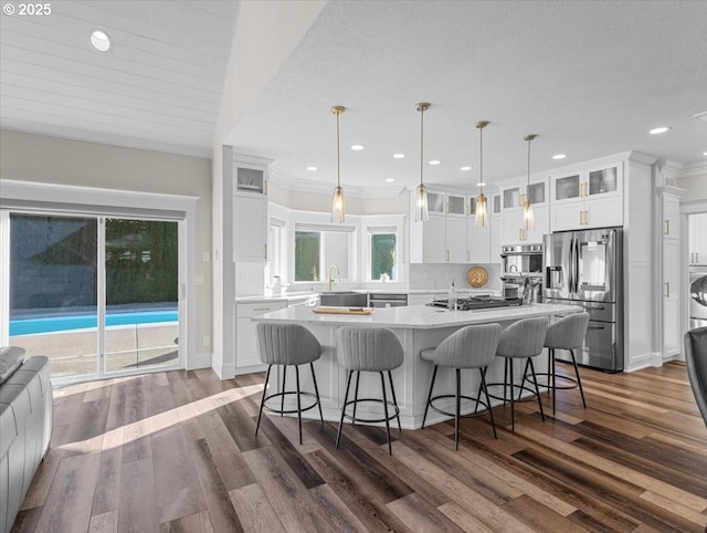 kitchen with lofted ceiling, decorative light fixtures, an island with sink, stainless steel appliances, and white cabinets