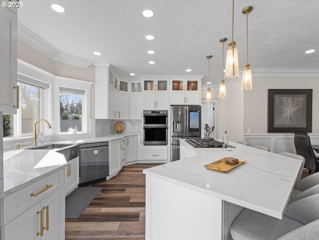 kitchen with a kitchen island, appliances with stainless steel finishes, a breakfast bar, white cabinetry, and crown molding