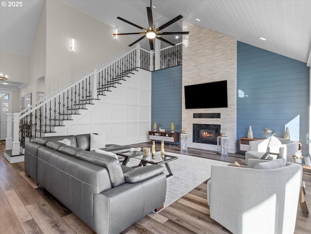 living room with hardwood / wood-style flooring, ceiling fan, high vaulted ceiling, a stone fireplace, and wooden ceiling