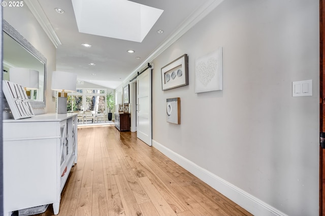 corridor featuring crown molding, a barn door, vaulted ceiling with skylight, and light hardwood / wood-style floors