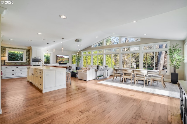 kitchen with lofted ceiling, decorative light fixtures, a center island with sink, and light wood-type flooring