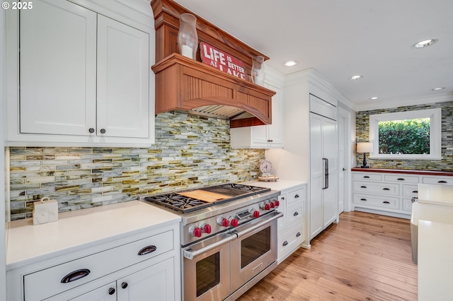 kitchen with high end appliances, white cabinetry, decorative backsplash, and light hardwood / wood-style flooring