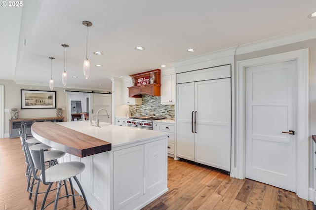 kitchen with high quality appliances, an island with sink, white cabinets, decorative light fixtures, and a barn door