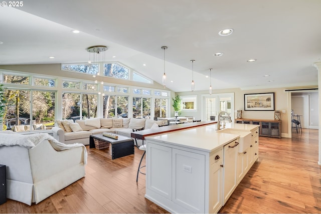 kitchen with white cabinetry, decorative light fixtures, vaulted ceiling, light hardwood / wood-style flooring, and an island with sink