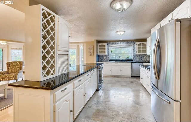 5706 SW Hamilton St, Portland, OR 97221 - kitchen with stainless steel appliances, dark countertops, glass insert cabinets, a textured ceiling, and white cabinetry