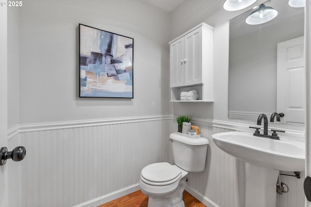 half bathroom with a wainscoted wall, a sink, toilet, and wood finished floors