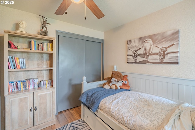 bedroom with a closet, a wainscoted wall, light wood-style flooring, and ceiling fan