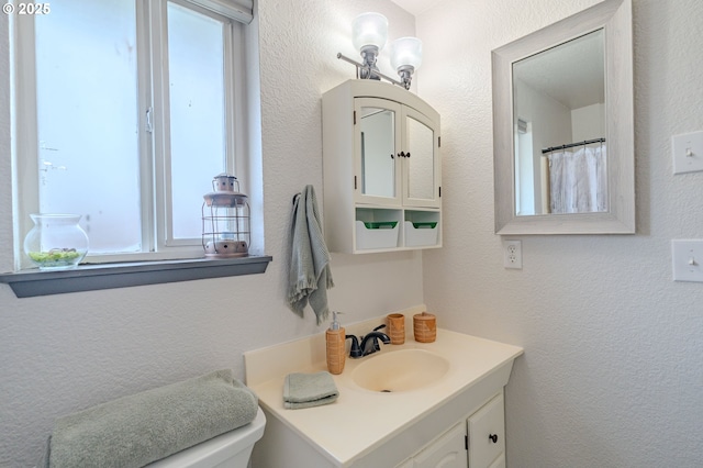 bathroom featuring toilet, vanity, and a textured wall