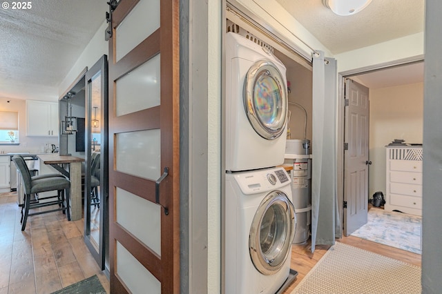 clothes washing area with light wood-type flooring, a barn door, a textured ceiling, and stacked washing maching and dryer