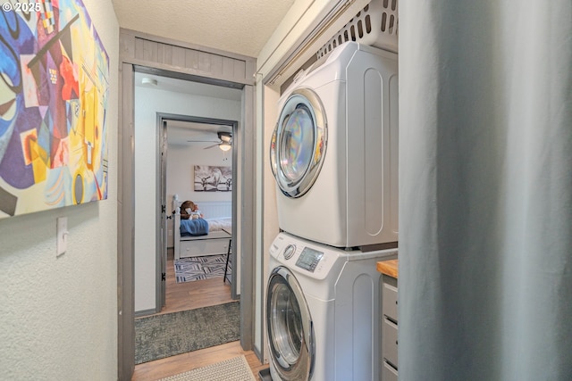 washroom featuring a textured ceiling, wood finished floors, stacked washer / dryer, ceiling fan, and laundry area