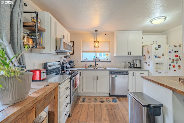 kitchen with light wood finished floors, wooden counters, a sink, white cabinets, and appliances with stainless steel finishes