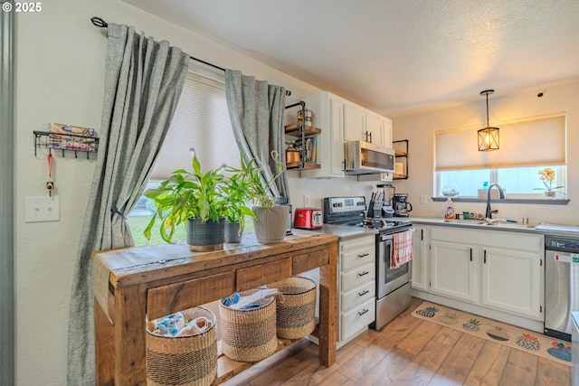 kitchen with a sink, appliances with stainless steel finishes, light wood-style flooring, and white cabinetry