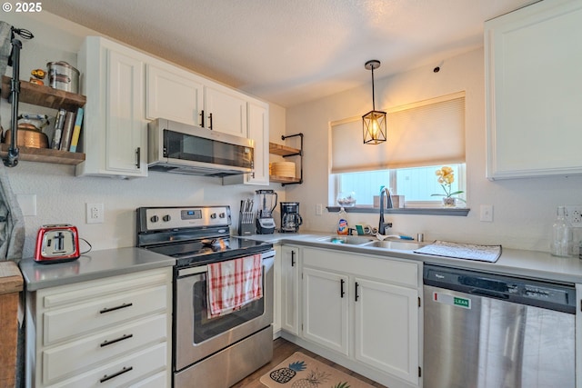 kitchen with open shelves, white cabinets, appliances with stainless steel finishes, and a sink