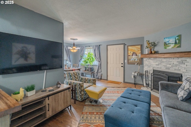 living area featuring a textured ceiling, a brick fireplace, wood finished floors, and a chandelier