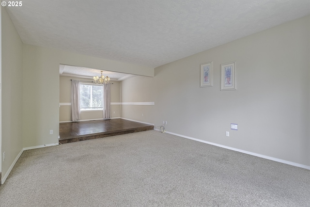 spare room with a chandelier, carpet, baseboards, and a textured ceiling