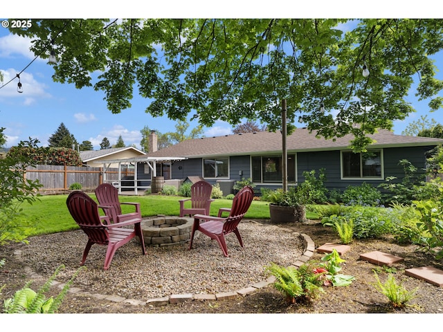 back of house featuring a chimney, a lawn, fence, an outdoor fire pit, and a shingled roof