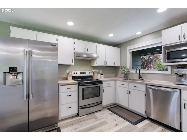 kitchen with light wood-style floors, under cabinet range hood, white cabinets, a sink, and appliances with stainless steel finishes
