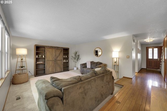 living area with light wood-style floors, baseboards, a textured ceiling, and visible vents